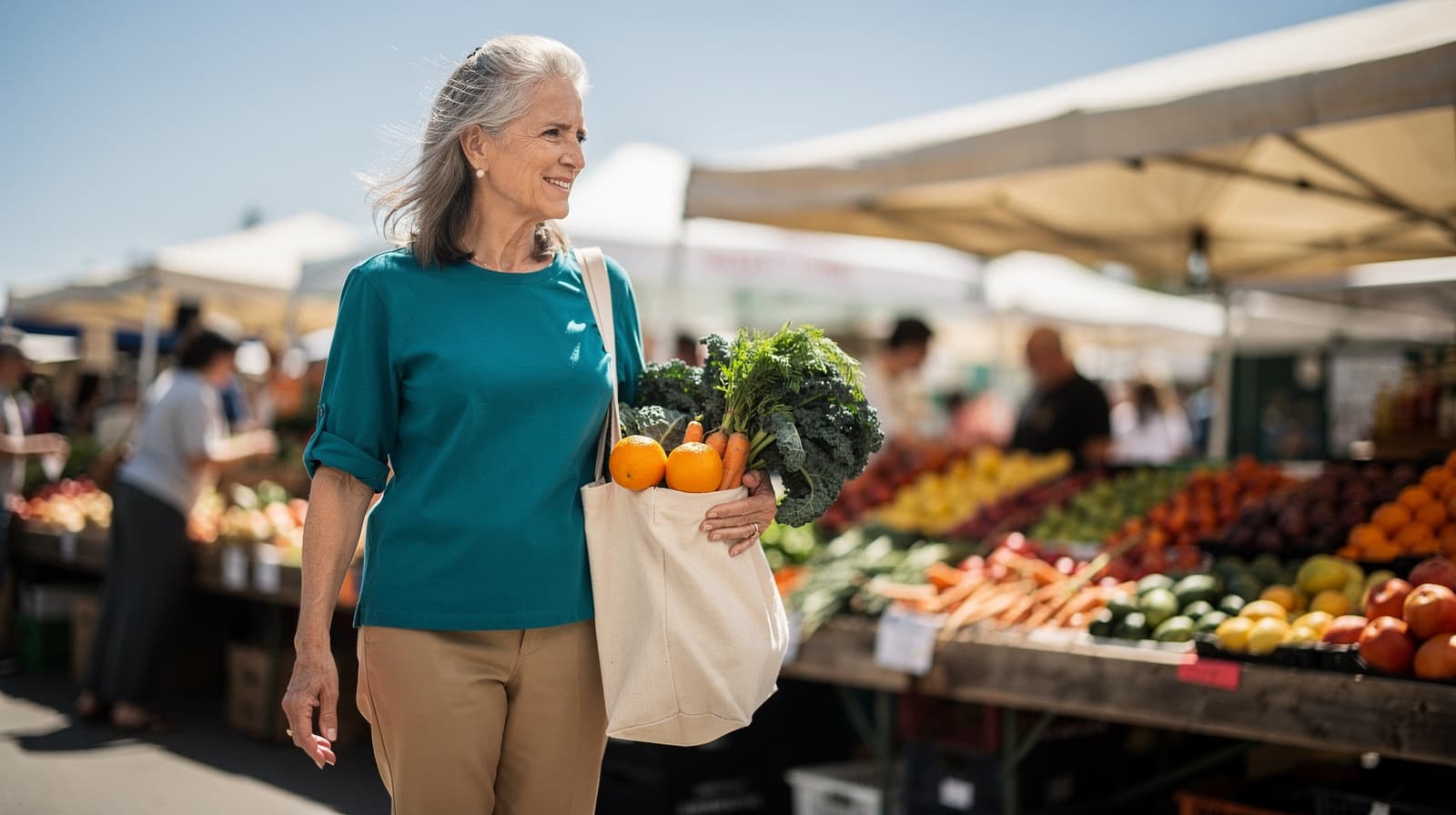 A woman carries a bag of fresh produce at an outdoor market with various fruits and vegetables displayed on tables.
