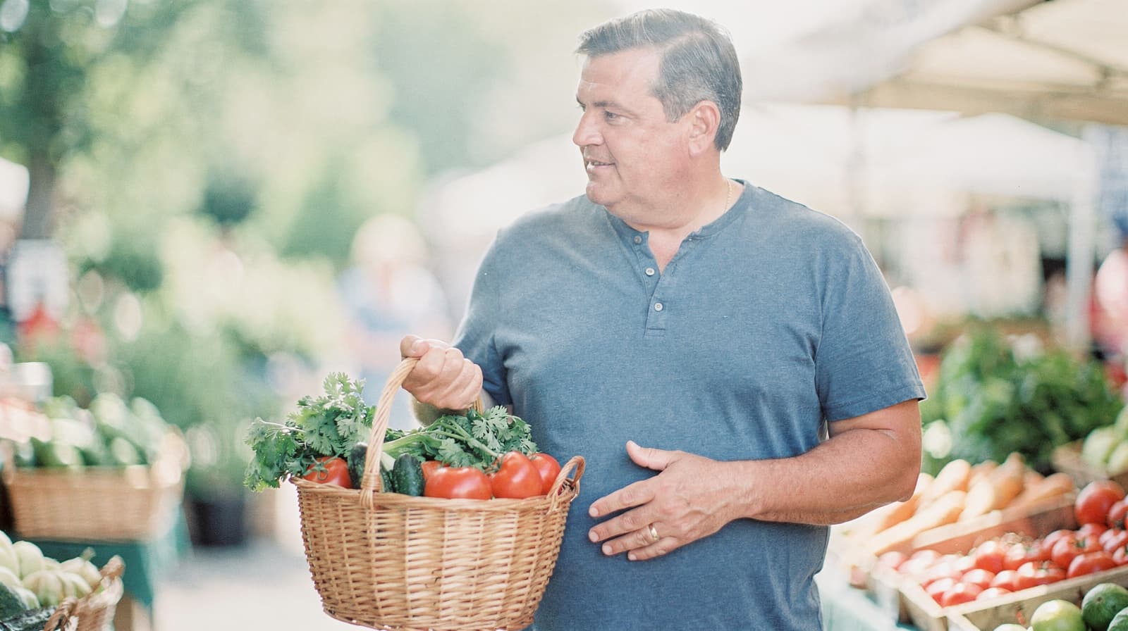 A man holds a basket of vegetables at an outdoor market.