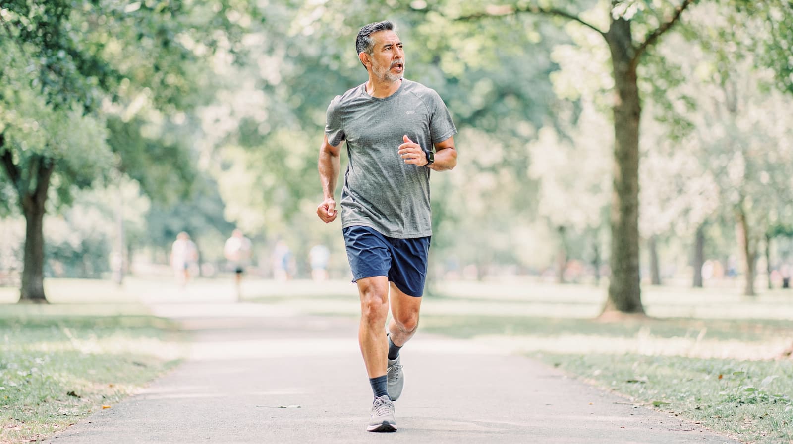 A man jogs on a tree-lined path in a park on a sunny day.