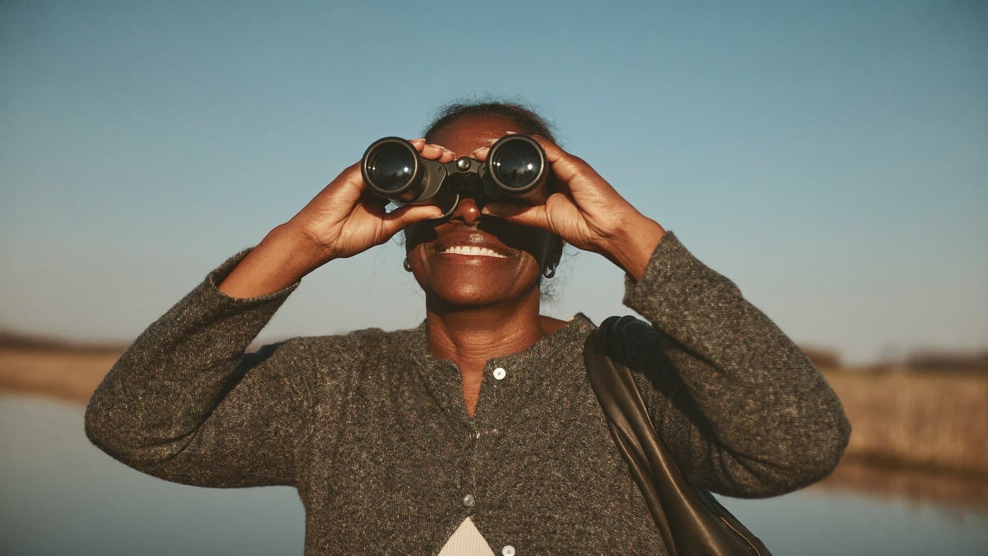 A woman looking through binoculars across an estuary on a clear day.