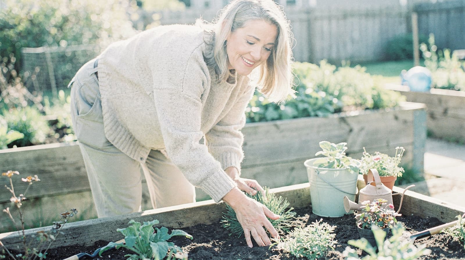 A woman tends to plants in a raised garden bed on a sunny day.