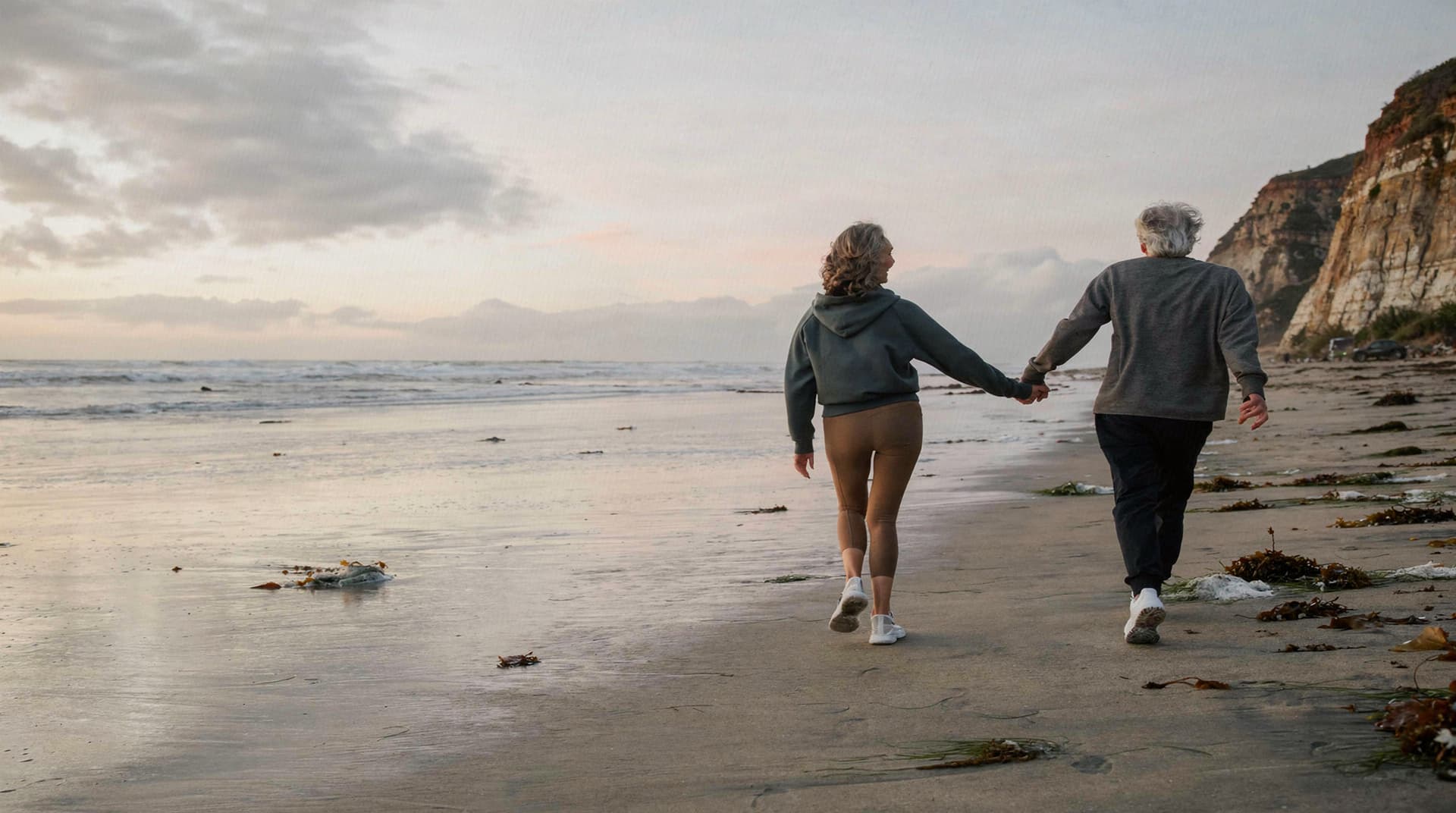 A man and a woman hold hands while walking along a sandy beach at sunset.