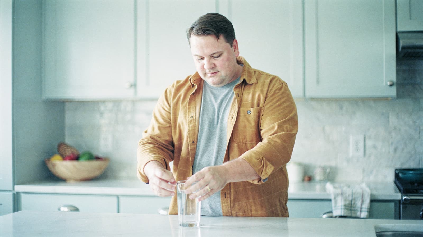 A man in a kitchen stirs a drink in a glass on a countertop.