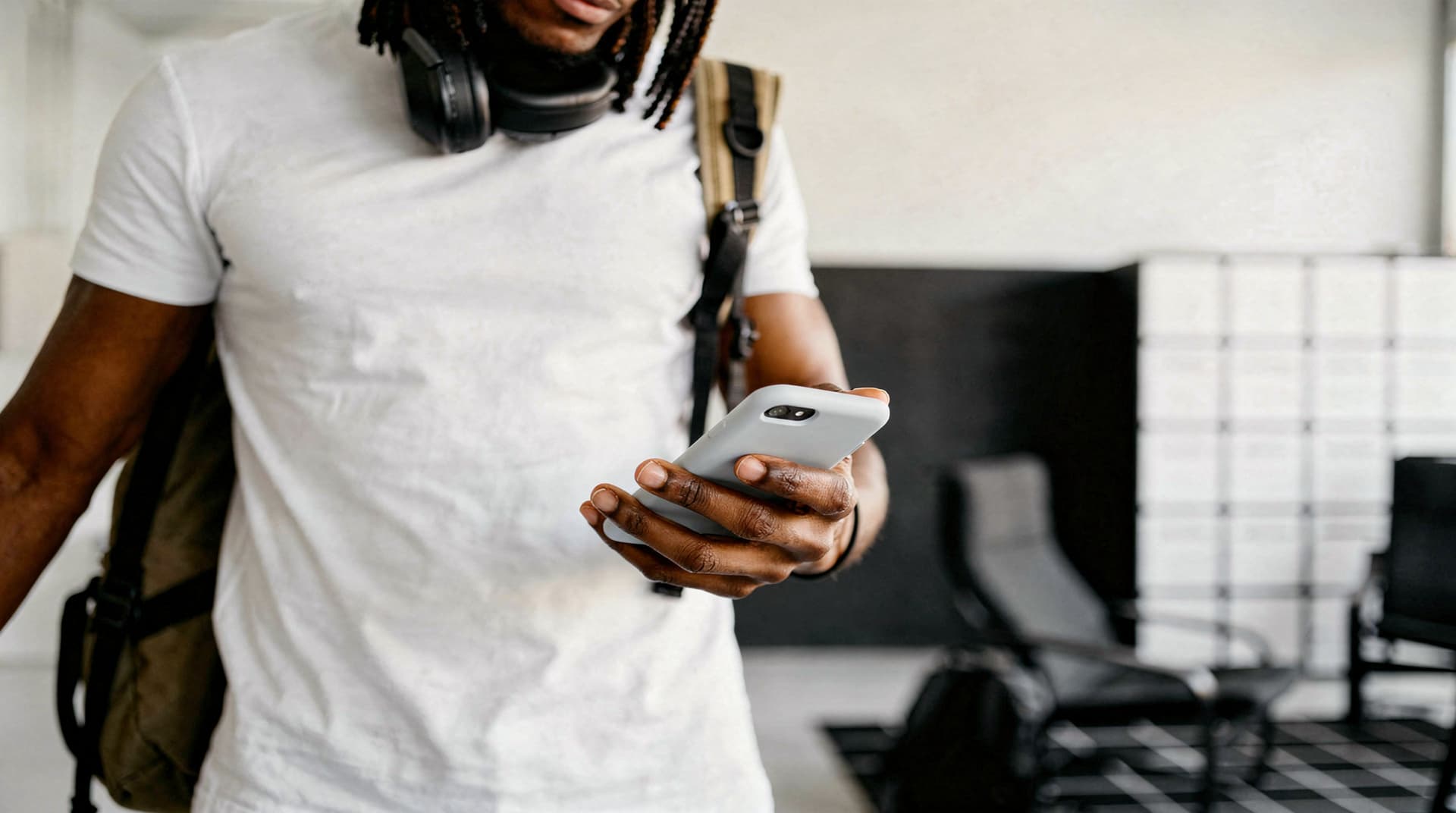 A person in a white shirt looks at a smartphone while standing in a modern office space.