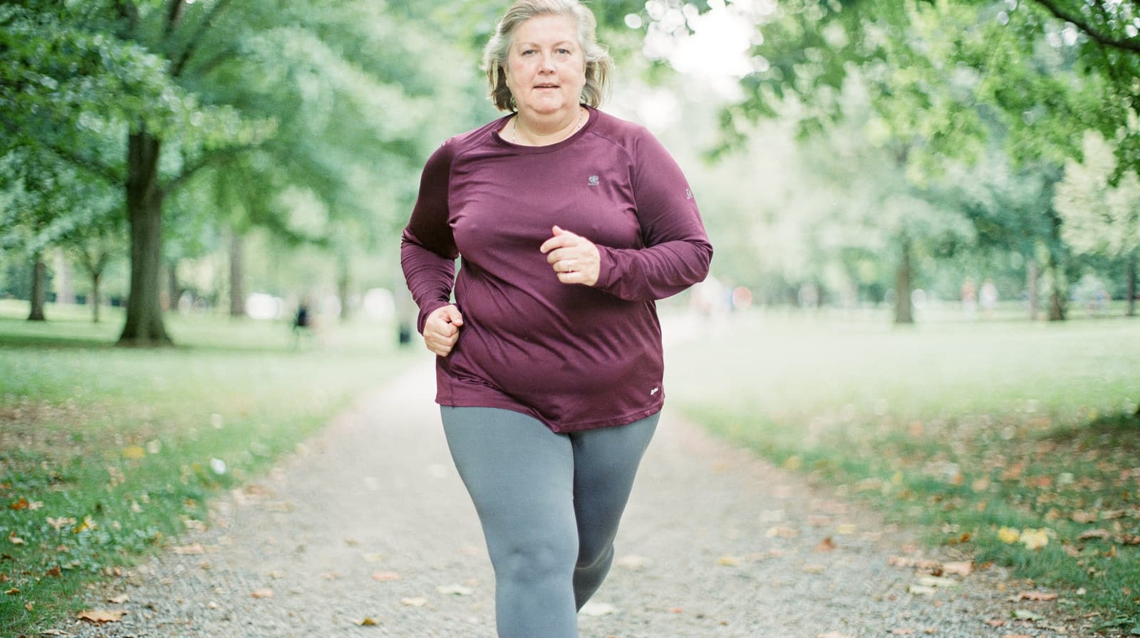 A woman jogs along a tree-lined path in a park.