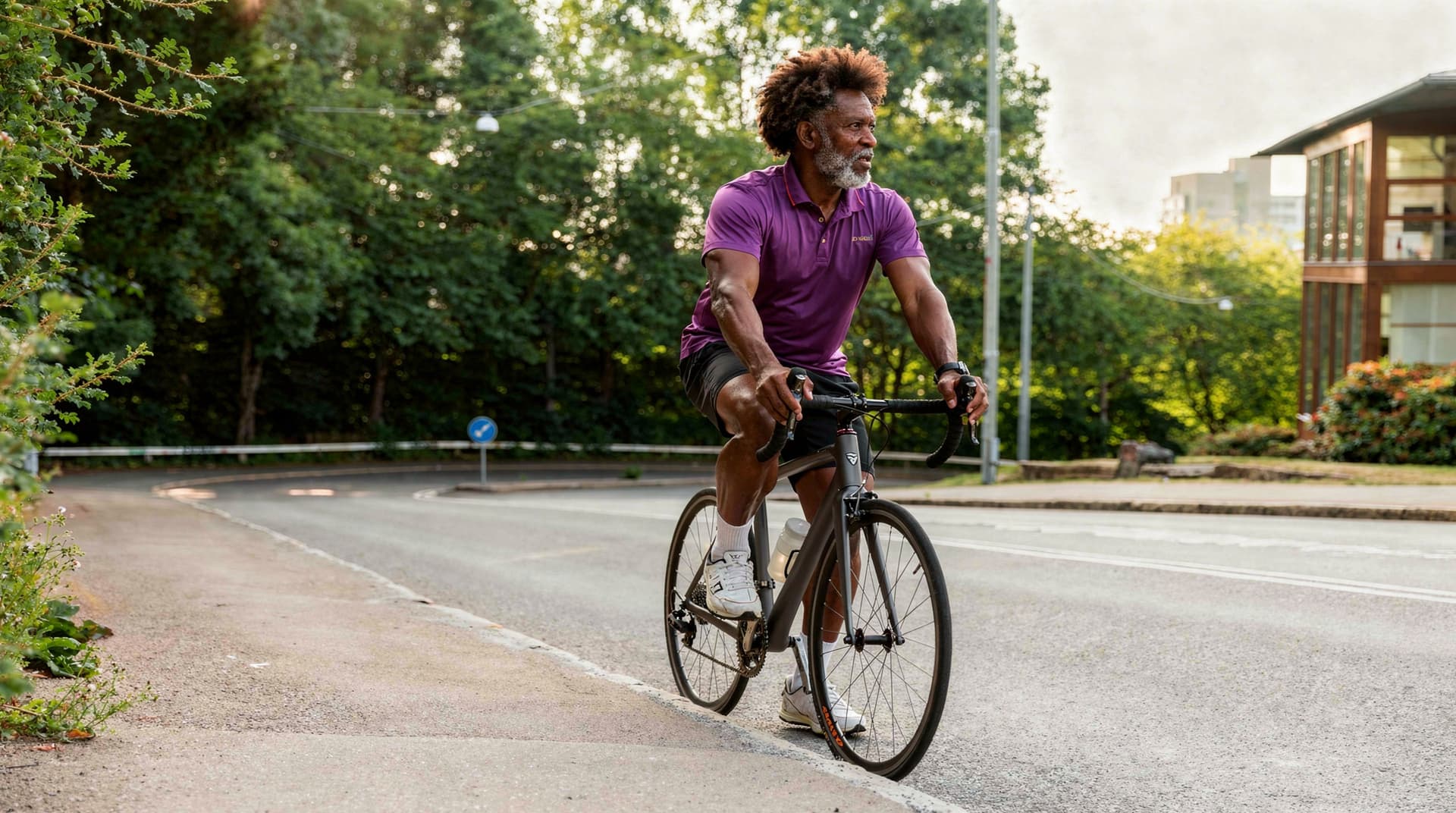 A man rides a bicycle on a road surrounded by trees and a building in the background.