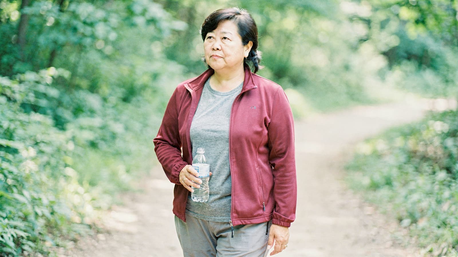 A woman walks on a forest trail holding a water bottle.