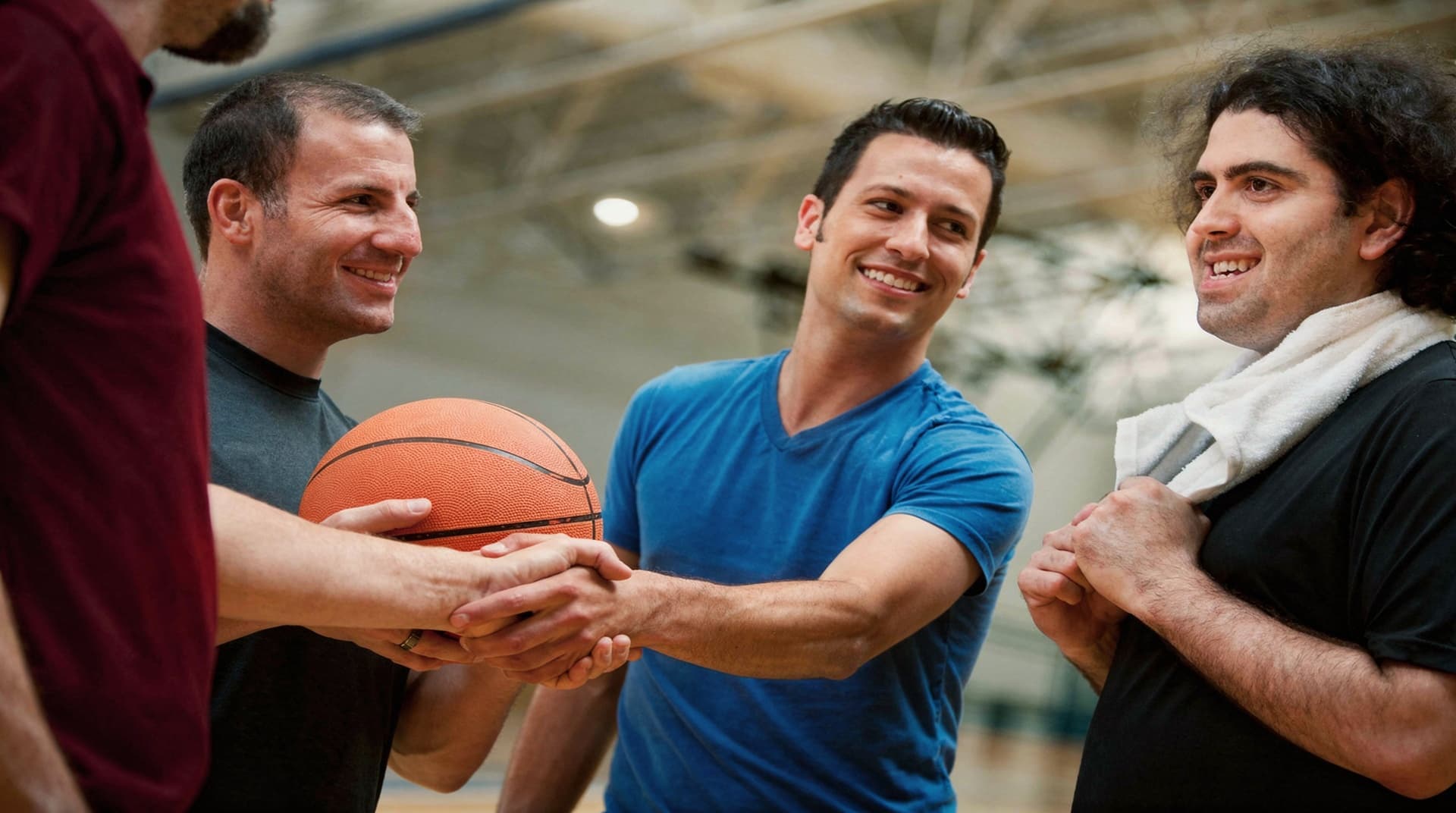 Four men stand in a gym, smiling and holding a basketball.