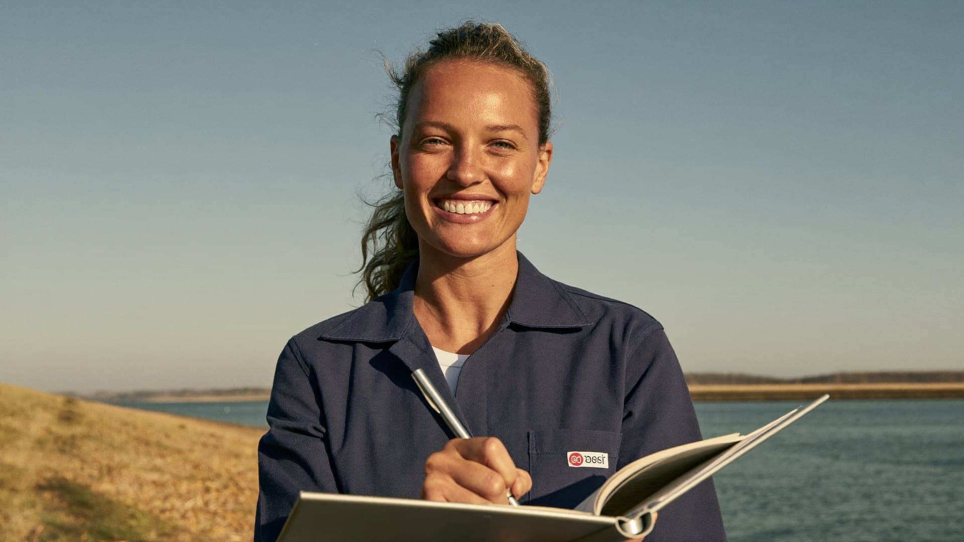 A woman making notes in a notebook outdoors in warm afternoon light.