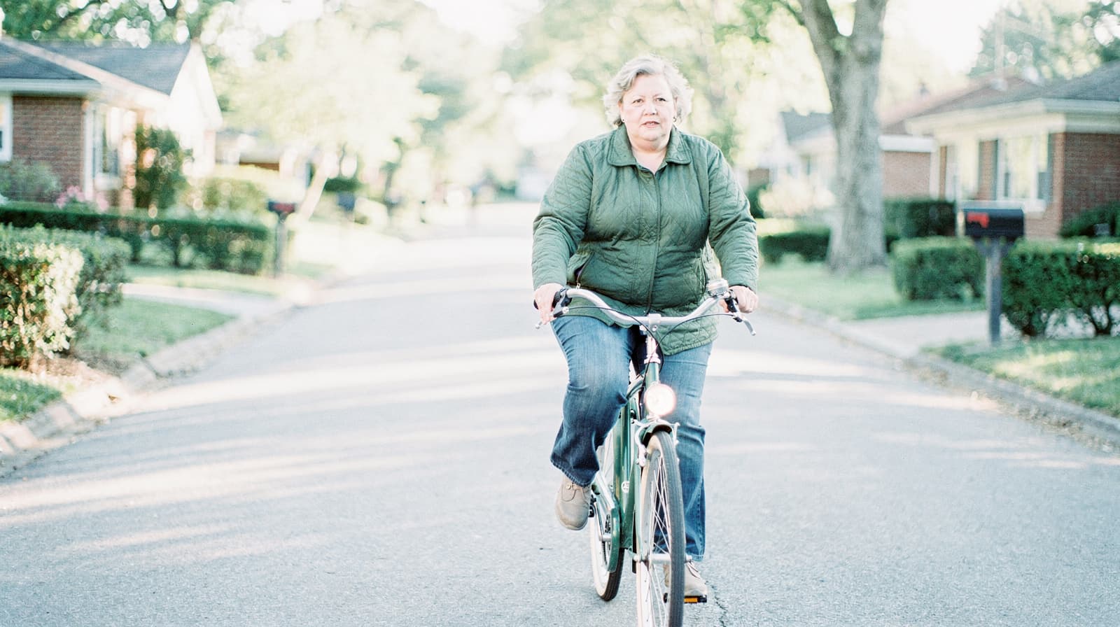A person rides a bicycle down a suburban street lined with houses and trees.