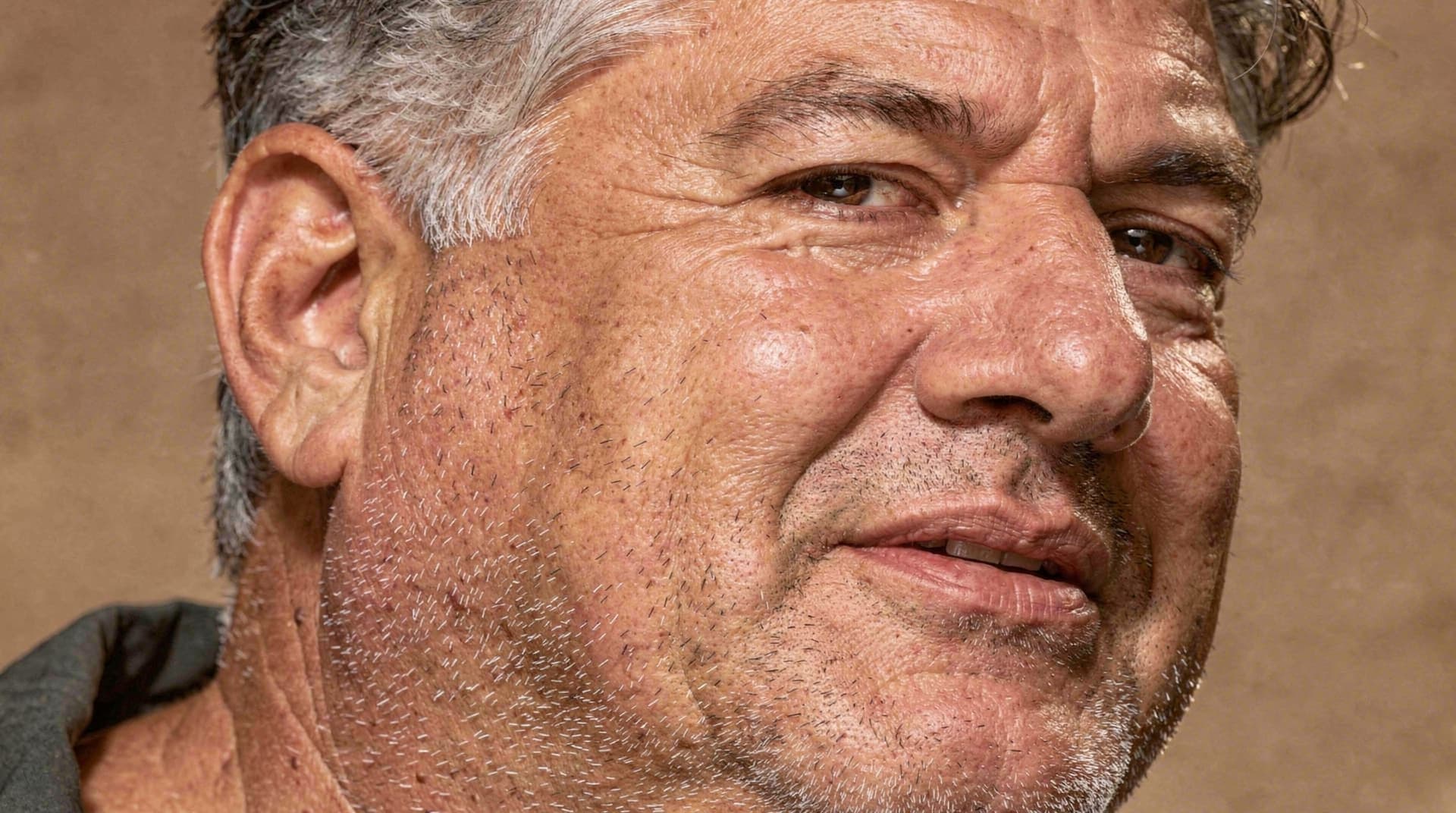 A man with short hair and stubble looks slightly to the side against a plain background.