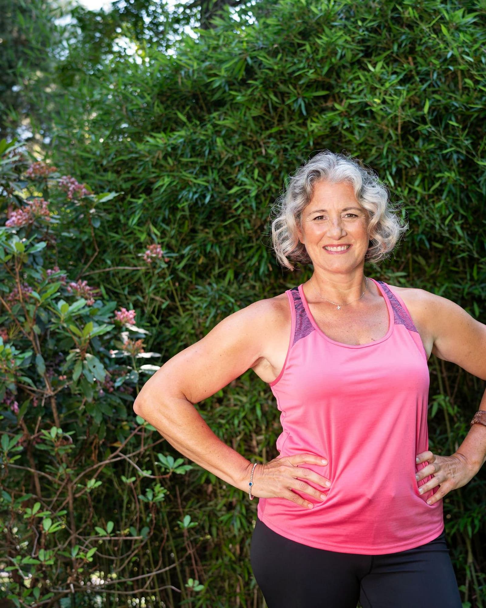 A strong, vital American woman in her mid fifties outdoors after a walk, hands on her hips, glowing.