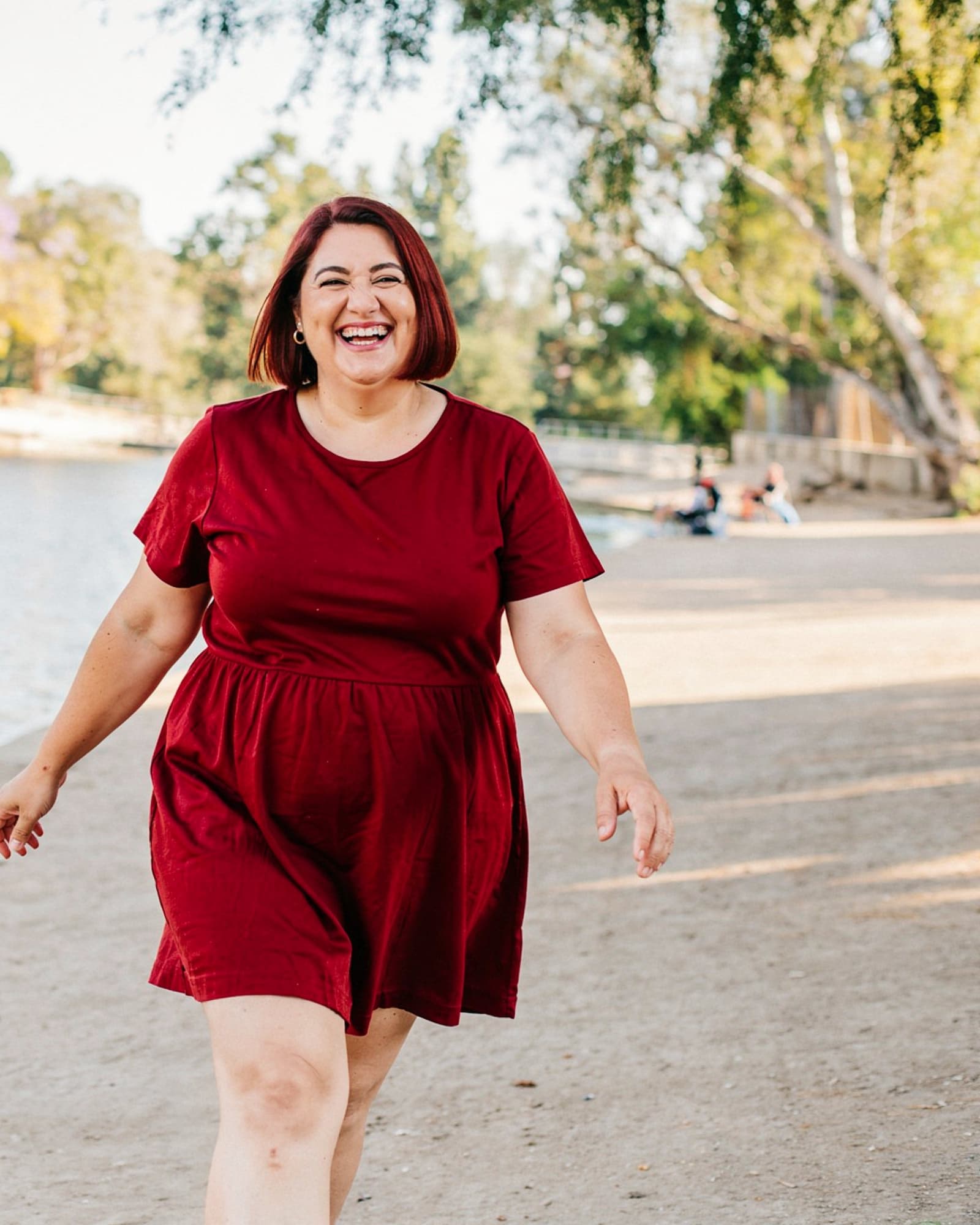 A joyful curvy American woman in her late forties laughing by a lake, vibrant and alive.