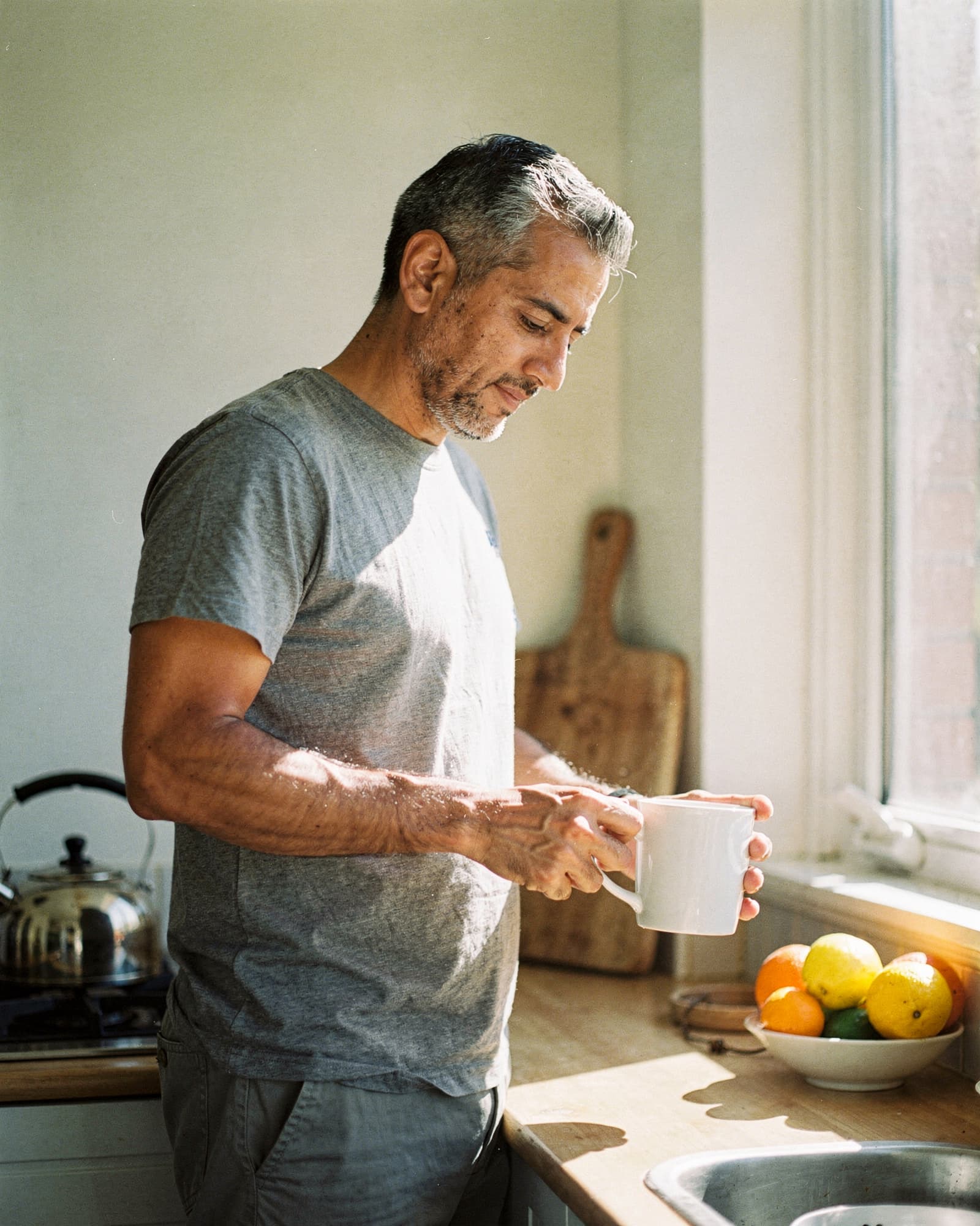 A lean man in his forties pouring coffee in a bright, sun-filled kitchen on an ordinary morning