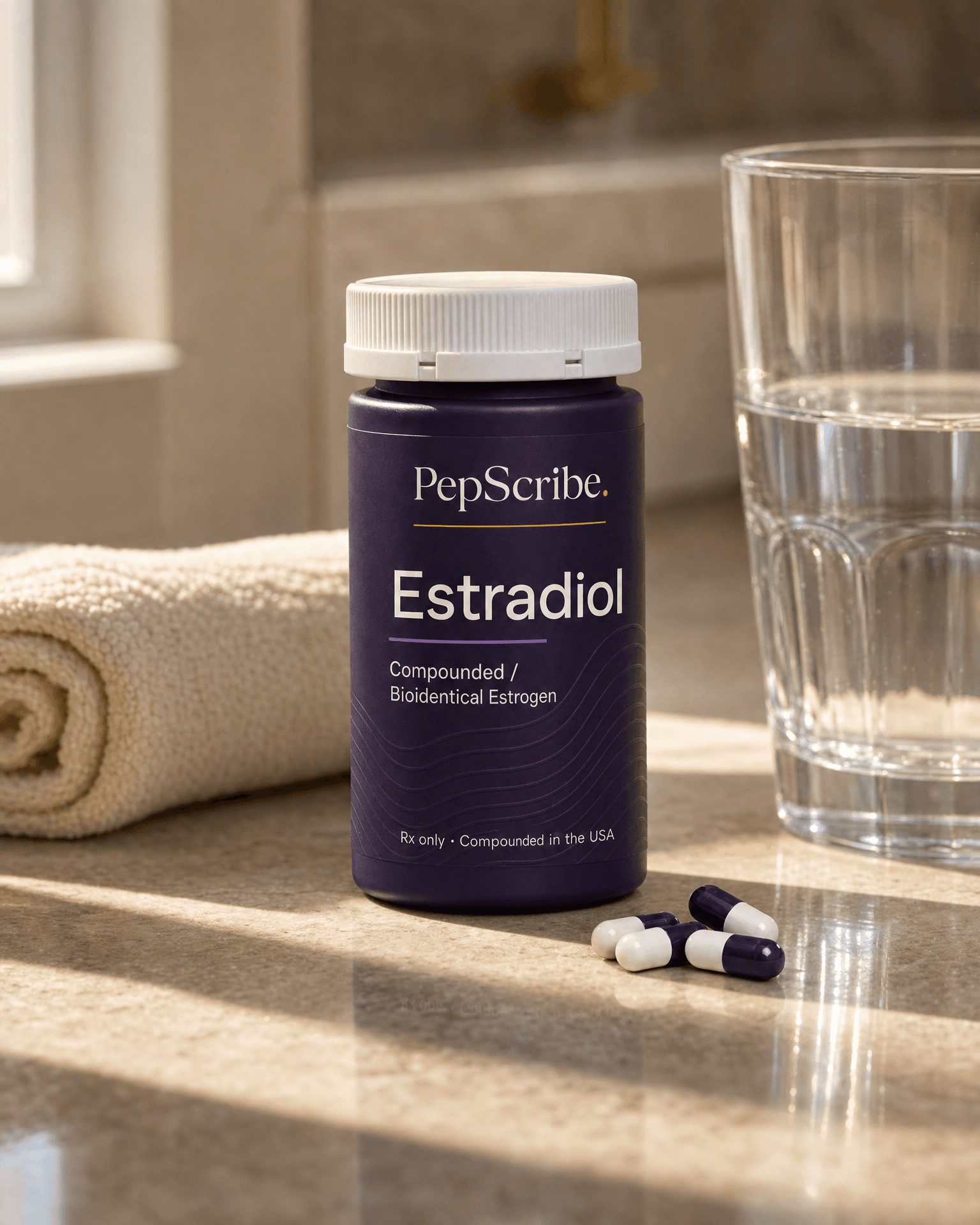 A PepScribe-branded compounded bioidentical estradiol capsule bottle on a sunlit bathroom counter beside a rolled towel and a glass of water.