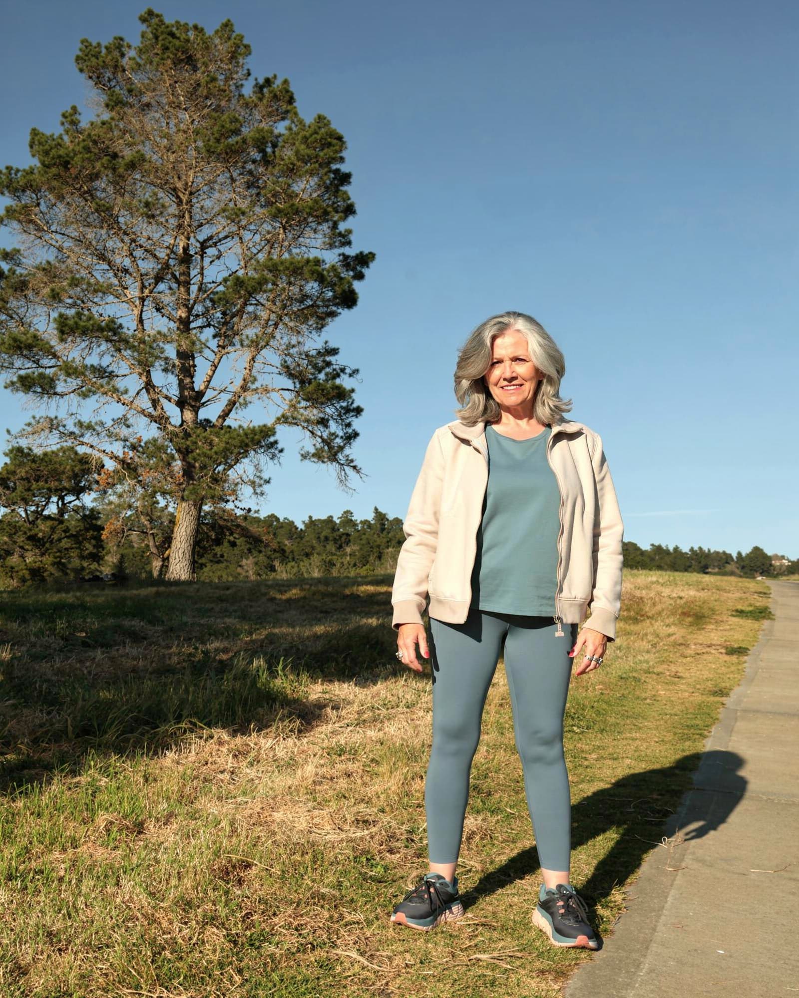 An American woman in her early fifties standing on an open path outdoors, serene and self-assured.