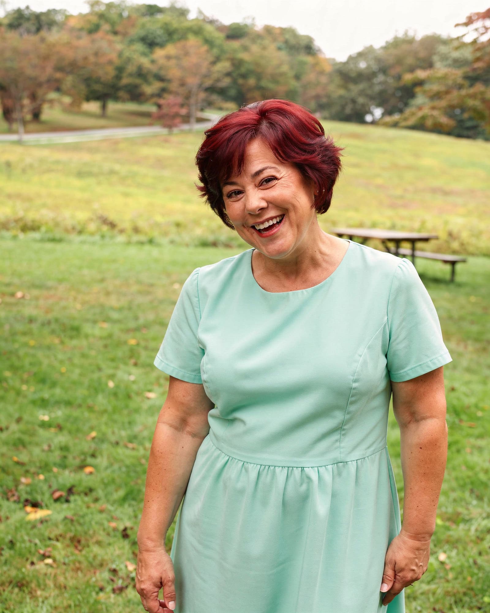 A radiant American woman in her late forties laughing in a sunny park, confident and glowing.