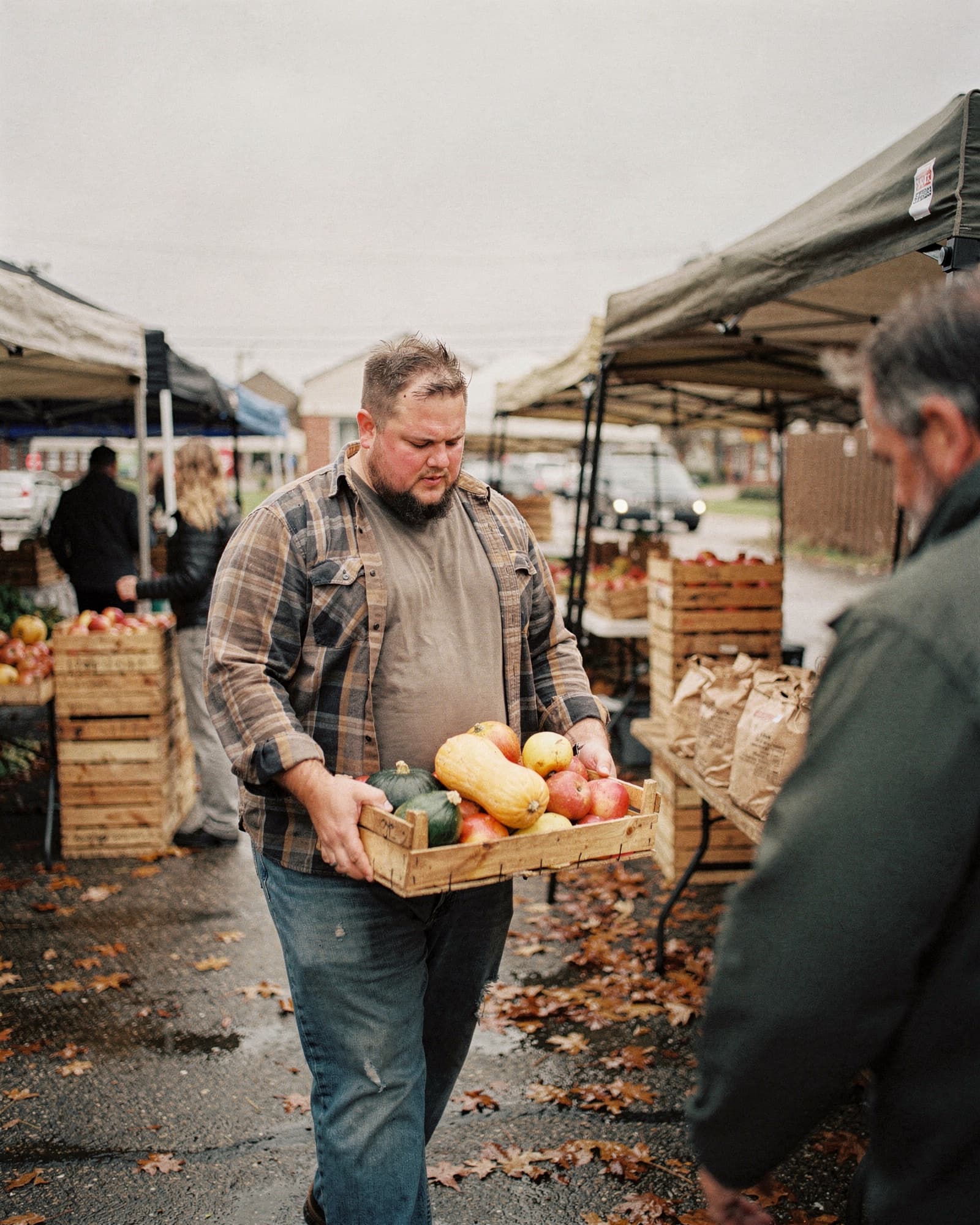 A heavyset man carrying a crate of produce at a Wisconsin farmers market in autumn
