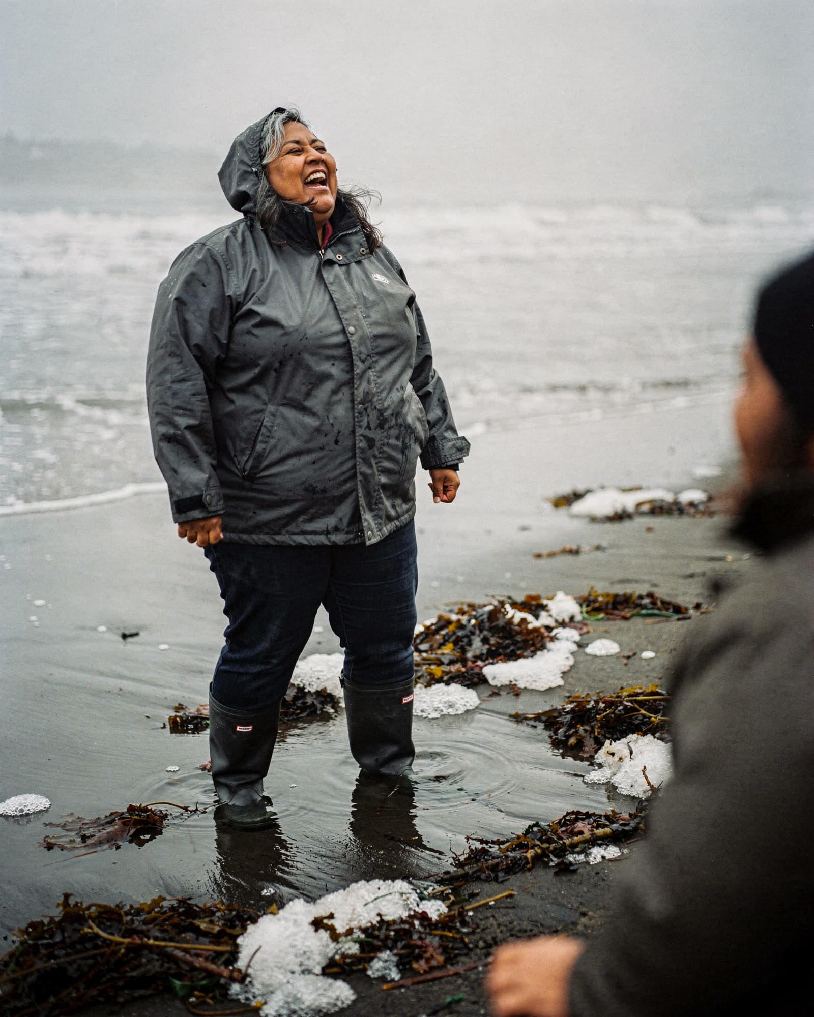 A plus-size woman laughing as she walks the tideline of a foggy Oregon beach in winter