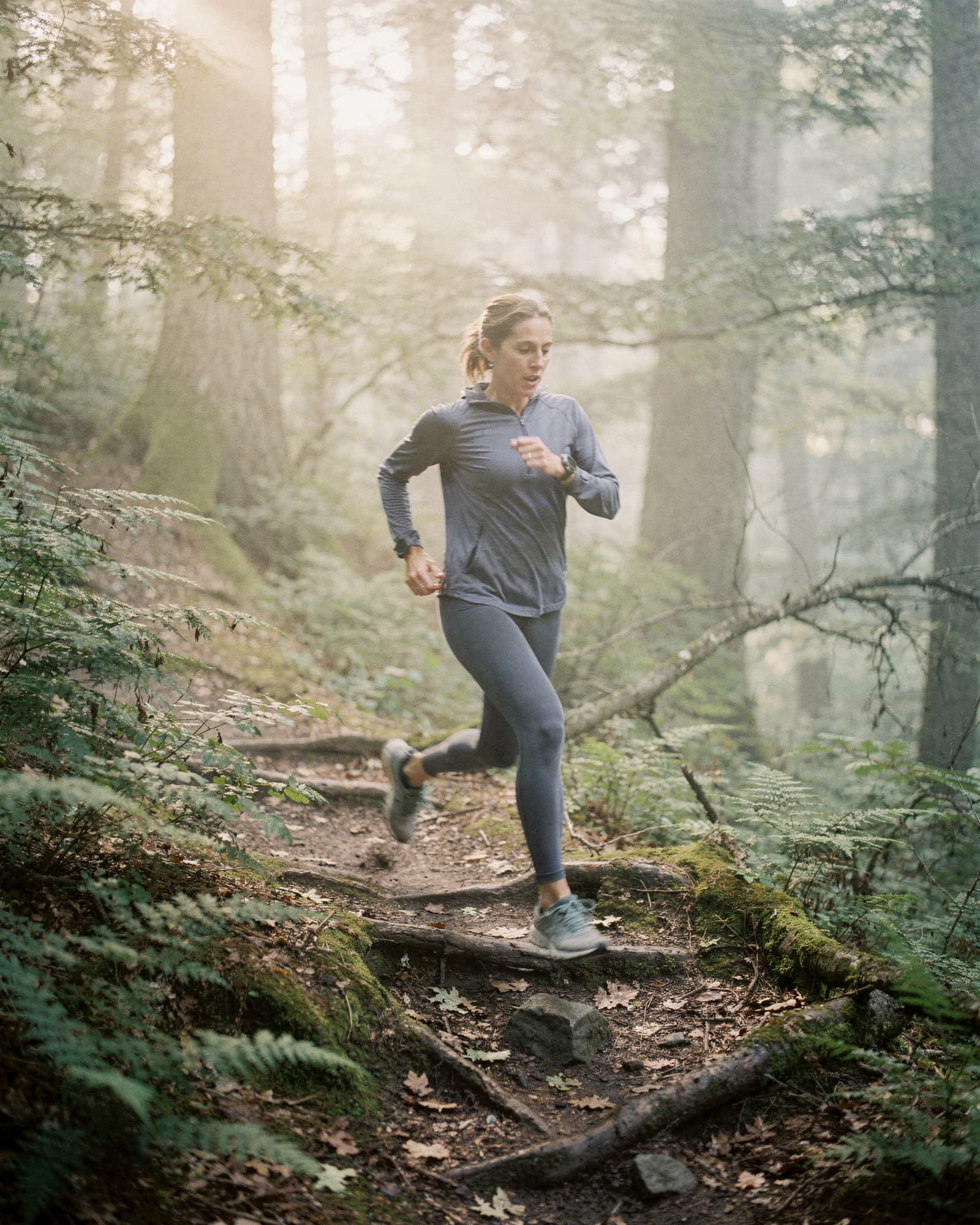 A lean woman on a sunrise trail run through a sun-dappled summer forest