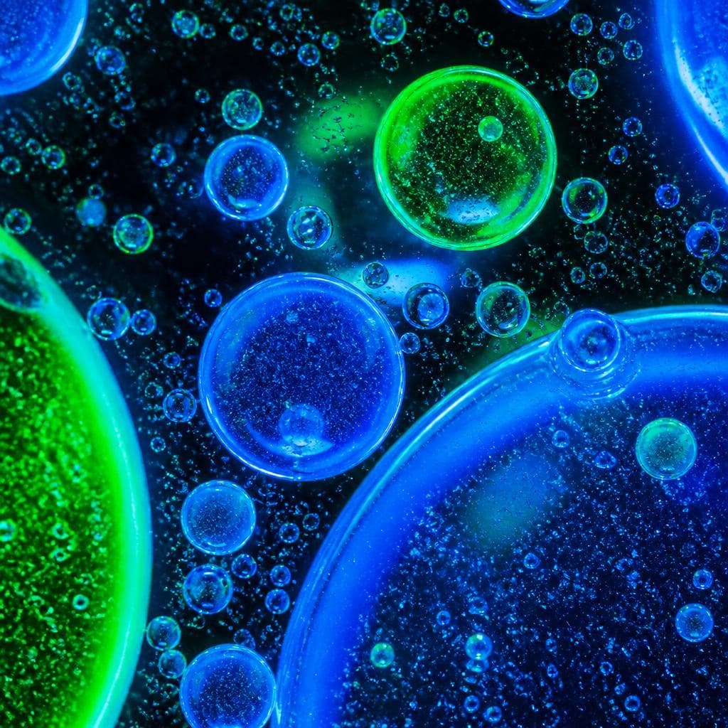 Vibrant macro of luminous serum droplets glowing in bright blue and green