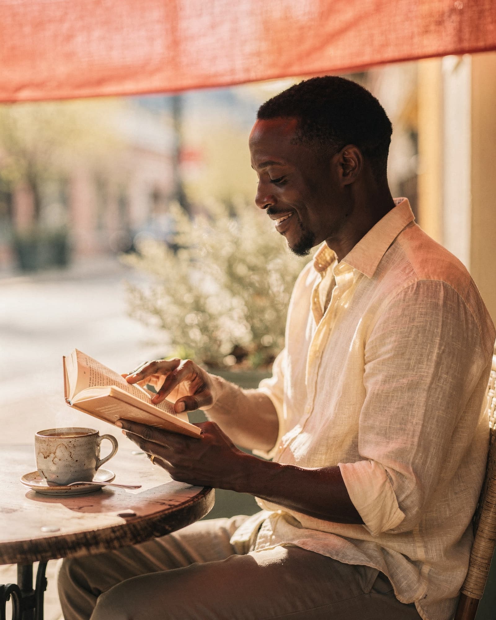 Man reading a paperback book at a sunlit cafe table on a spring afternoon