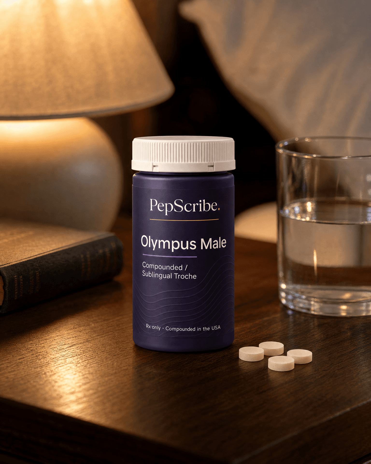 A PepScribe-branded Olympus Male compounded sublingual troche bottle on a warm walnut nightstand beside a lamp, a book and a glass of water.