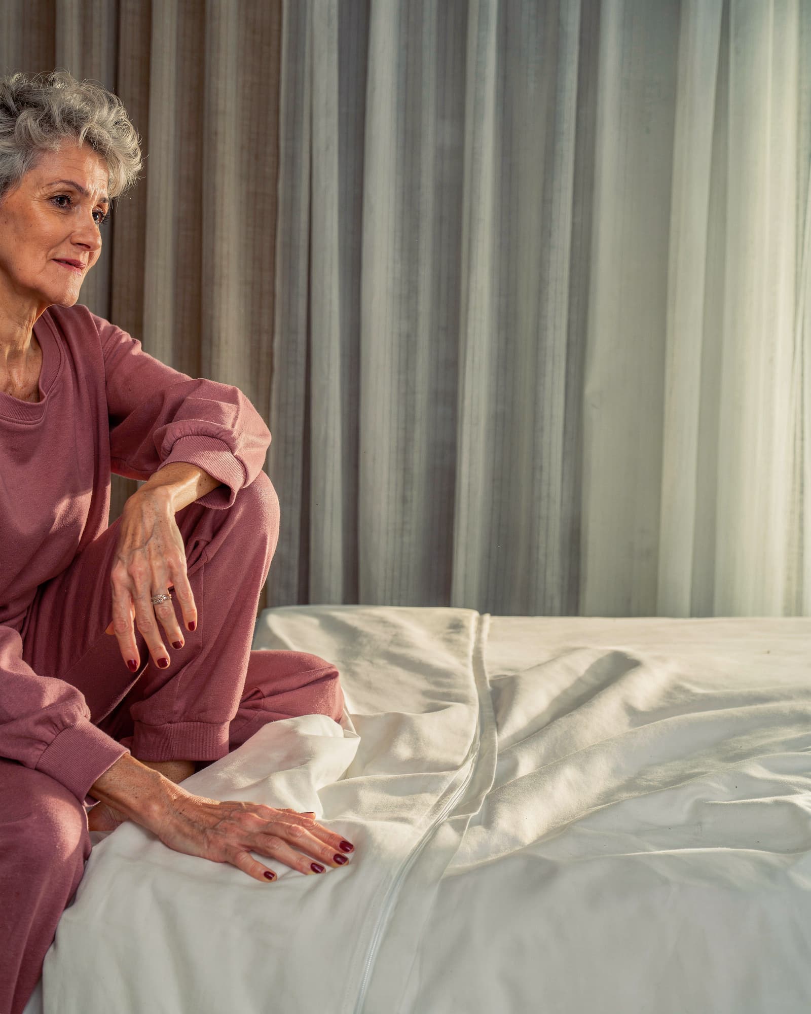 An American woman in her early fifties waking gently at the edge of her bed in soft morning light, calm and rested.