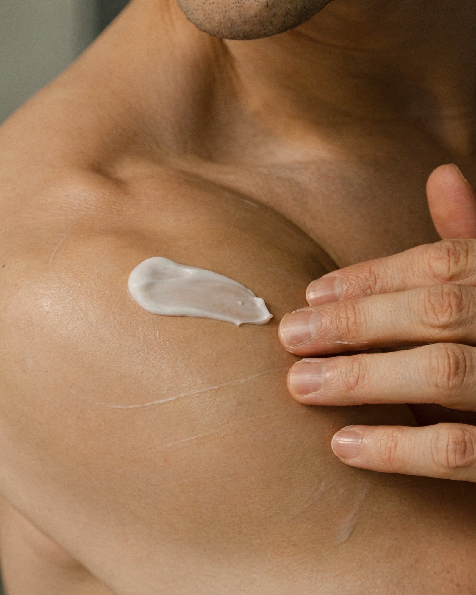 A man smoothing a measured dose of compounded testosterone cream onto his shoulder in soft window light.