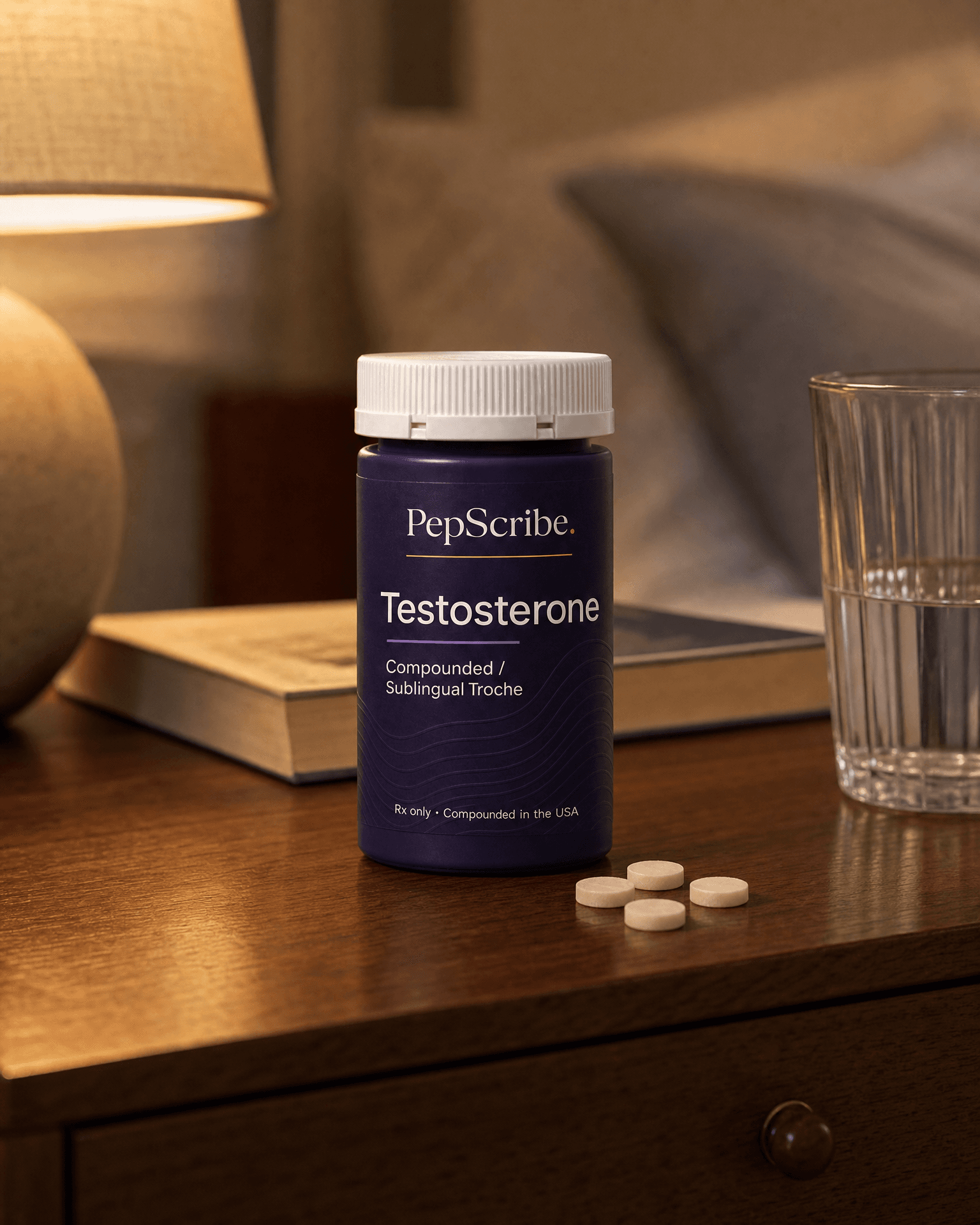 A PepScribe-branded compounded testosterone sublingual troche bottle on a warm walnut nightstand beside a lamp, a book and a glass of water.