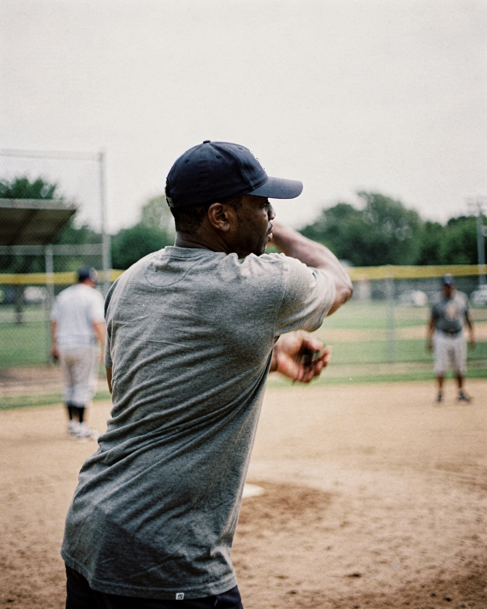 A man throwing during a pickup baseball game on an overcast afternoon